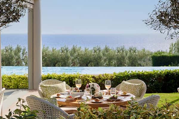 Outdoor dining area at Ikos Oceania with a table set for four, offering views of an infinity pool and the Aegean Sea.