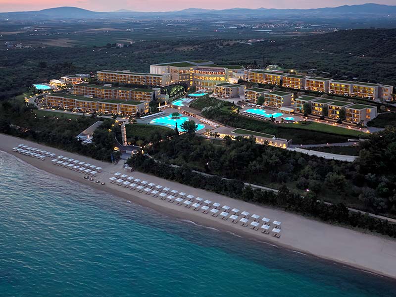 Aerial view of Ikos Oceania resort at sunset in Halkidiki, Greece, showcasing pools, gardens, and a beachfront with sun loungers.