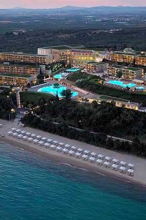 Aerial view of Ikos Oceania resort at sunset in Halkidiki, Greece, showcasing pools, gardens, and a beachfront with sun loungers.