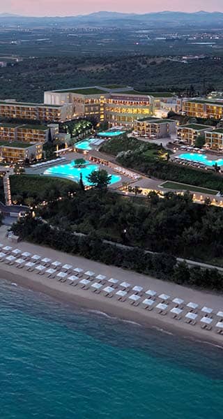Aerial view of Ikos Oceania resort at sunset in Halkidiki, Greece, showcasing pools, gardens, and a beachfront with sun loungers.