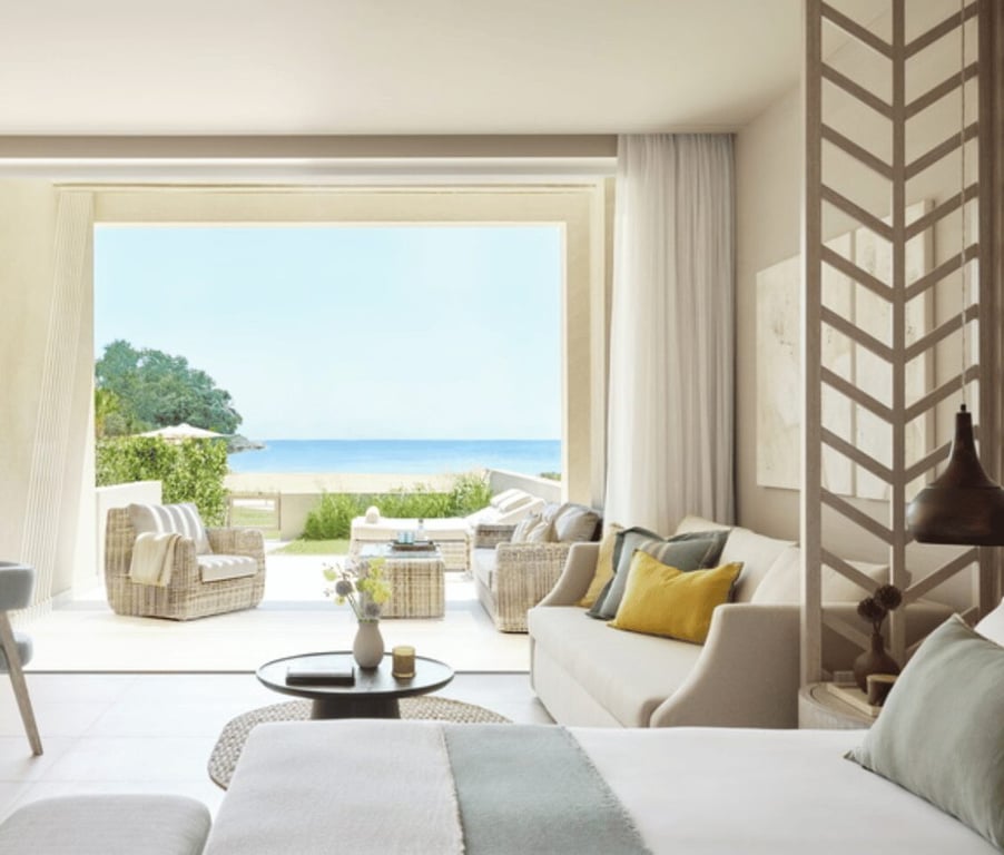 Deluxe Junior Bungalow Suite at Ikos Odisia, featuring a private garden and sea view through large sliding doors, with elegant interior seating and decor in soft colours.