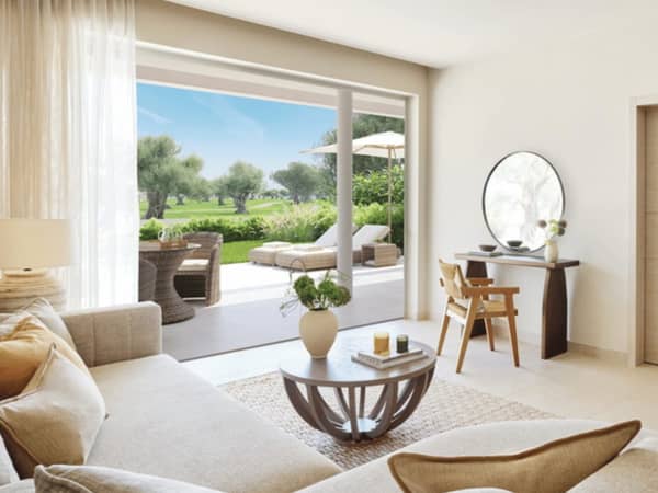 Living room of Ikos Odisia Deluxe Two Bedroom Bungalow Suite with garden view, featuring a comfortable sofa, coffee table, and access to a private garden with outdoor seating.