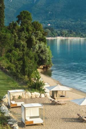 Ikos Odisia Beach with sun loungers and umbrellas, lush greenery, and mountains in the background.