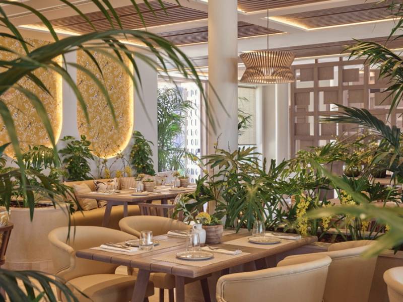Indoor restaurant at Ikos Odisia resort with elegantly set tables, lush greenery, and modern lighting.