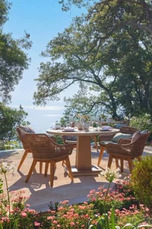 Outdoor dining area at Ikos Odisia Gallery with wicker chairs, wooden tables, surrounded by greenery and a sea view.