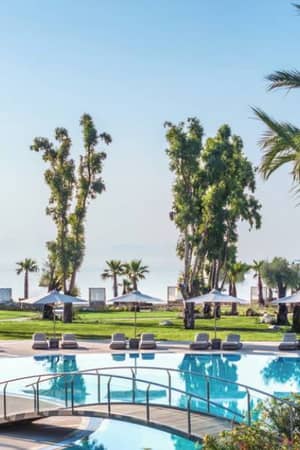 Pool area at Ikos Odisia resort with palm trees, sun loungers, and a view of the beach and sea.