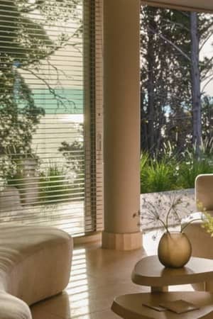 Ikos Odisia spa lounge area with curved seating, a coffee table with flowers, and large windows overlooking greenery and the sea.