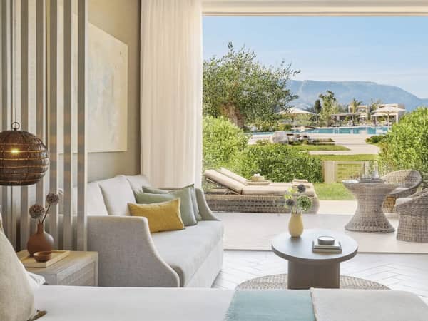 Ikos Odisia junior suite with a private garden, featuring a modern interior, outdoor seating, and a view of the pool.