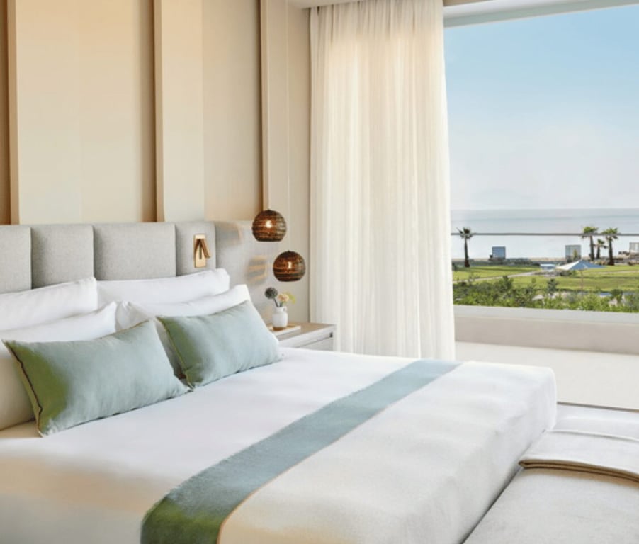 Elegant bedroom in a bungalow suite with a king-size bed, modern decor, and a balcony view of a pool at Ikos Odisia.