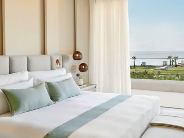 Elegant bedroom in a bungalow suite with a king-size bed, modern decor, and a balcony view of a pool at Ikos Odisia.