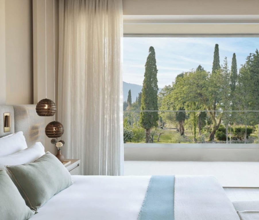 One-bedroom suite at Ikos Odisia with a garden view through a large window, featuring a comfortable bed and elegant decor.