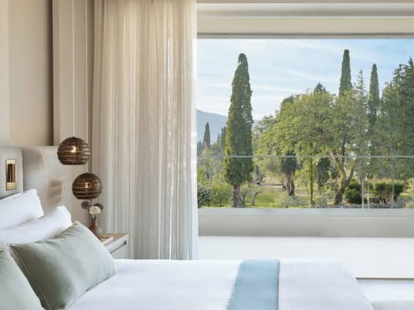 One-bedroom suite at Ikos Odisia with a garden view through a large window, featuring a comfortable bed and elegant decor.