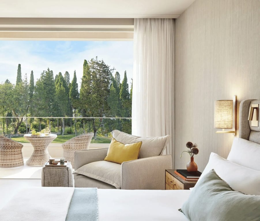 Ikos Odisia resort superior garden view room with elegant furnishings, including a bed and armchair, and a balcony overlooking greenery.