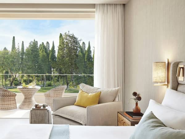 Ikos Odisia resort superior garden view room with elegant furnishings, including a bed and armchair, and a balcony overlooking greenery.