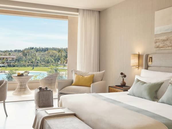 Interior of Ikos Odisia hotel room with pool view, featuring a large bed and a cosy seating area with a backdrop of greenery.
