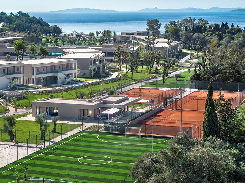 Luxury resort with clay and artificial grass tennis courts near the Ionian Sea, surrounded by modern villas and greenery.