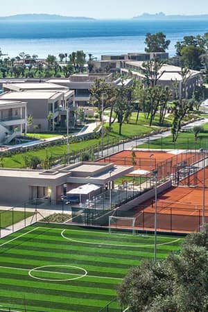 Luxury resort with clay and artificial grass tennis courts near the Ionian Sea, surrounded by modern villas and greenery.