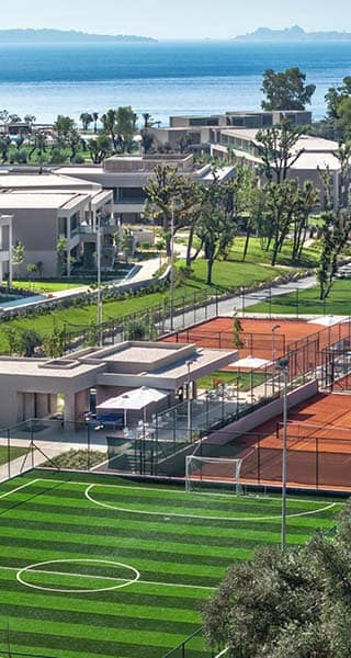 Luxury resort with clay and artificial grass tennis courts near the Ionian Sea, surrounded by modern villas and greenery.