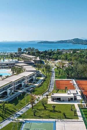 Aerial view of Ikos Odisia resort featuring tennis courts, a pool area, lush gardens, and the Ionian Sea.