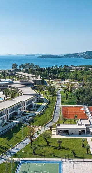 Aerial view of Ikos Odisia resort featuring tennis courts, a pool area, lush gardens, and the Ionian Sea.