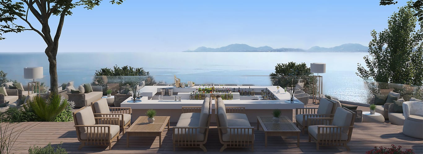 Outdoor terrace at Ikos Odisia resort, showcasing sea views with wicker furniture and greenery, calm sea and distant mountains visible under a clear sky.