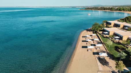 Aerial view of Ikos Olivia resort in Greece with beachfront villas, white sand beach, and turquoise waters.