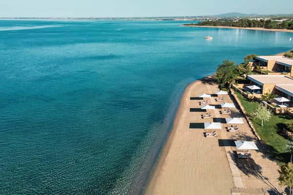 Aerial view of Ikos Olivia resort in Greece with beachfront villas, white sand beach, and turquoise waters.