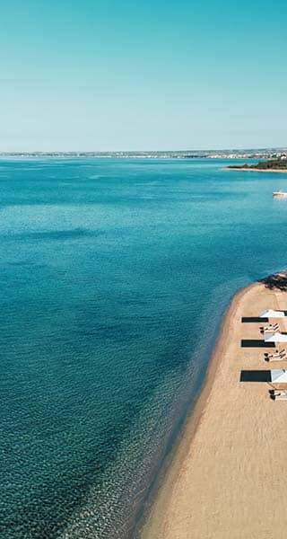 Aerial view of Ikos Olivia Resort's beach with sun loungers, parasols, and clear Aegean Sea waters.