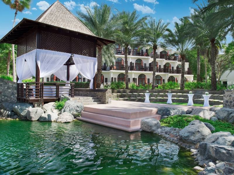 Amphitheatre at JA Palm Tree Court in Dubai, featuring a gazebo with white curtains, surrounded by a water feature and lush gardens with palm trees.