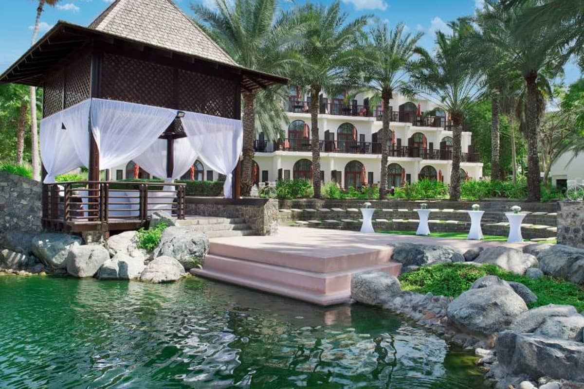 Amphitheatre at JA Palm Tree Court in Dubai, featuring a gazebo with white curtains, surrounded by a water feature and lush gardens with palm trees.