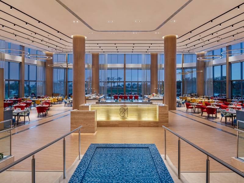 Stylish dining area at the JA Gallery with modern decor, red and yellow chairs, circular lights, and a prominent wooden panel centrepiece.