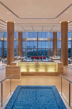 Stylish dining area at the JA Gallery with modern decor, red and yellow chairs, circular lights, and a prominent wooden panel centrepiece.