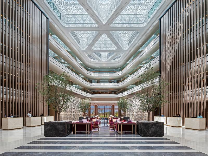 Luxurious lobby of JA Gallery with high ceiling, marble floors, stylish seating, and decorative greenery.