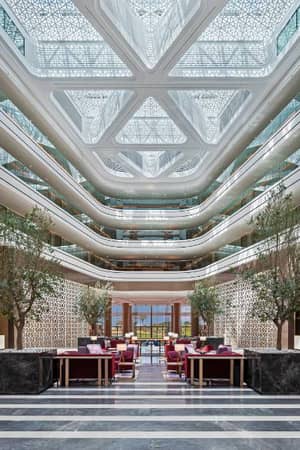 Luxurious lobby of JA Gallery with high ceiling, marble floors, stylish seating, and decorative greenery.