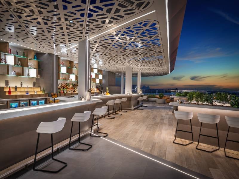 Outdoor bar at JA Gallery with modern seating, ambient lighting, and a scenic sunset view of the city.