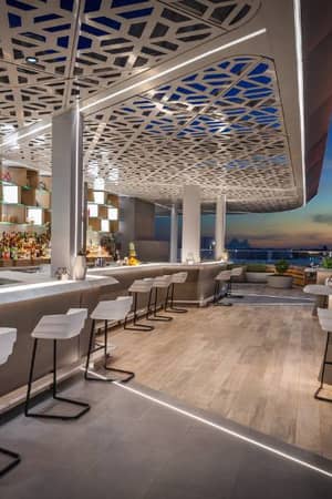 Outdoor bar at JA Gallery with modern seating, ambient lighting, and a scenic sunset view of the city.