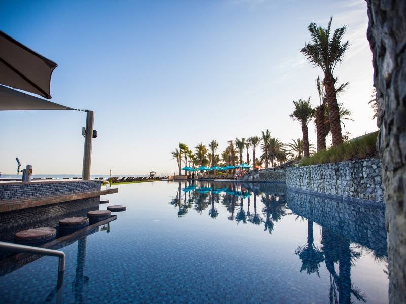 Infinity pool at JA Gallery Resort with ocean view, palm trees, and sun loungers.