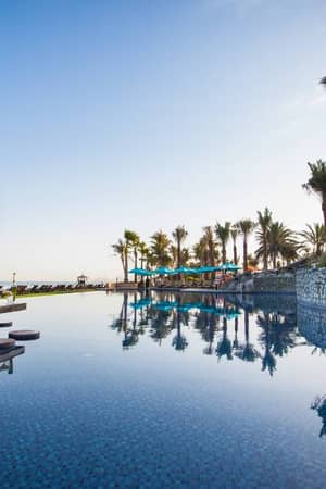 Infinity pool at JA Gallery Resort with ocean view, palm trees, and sun loungers.
