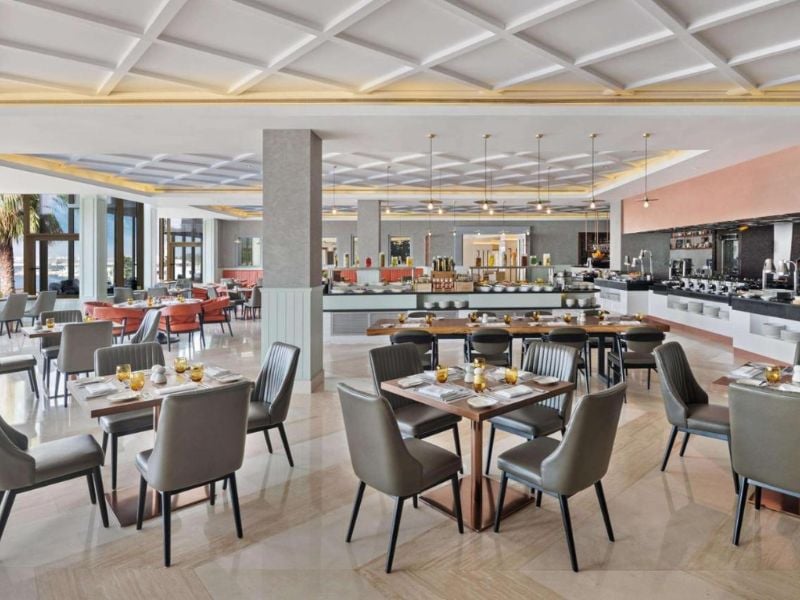Elegant restaurant interior with a large dining area, contemporary decor, neatly set tables, and a buffet counter in the background.