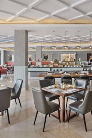 Elegant restaurant interior with a large dining area, contemporary decor, neatly set tables, and a buffet counter in the background.