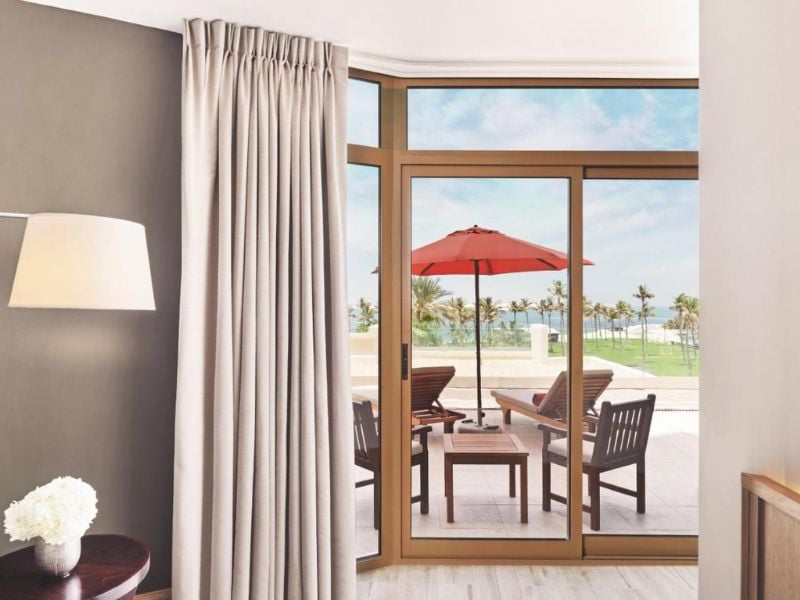 Hotel room at JA Resort with a large window opening to a patio with red umbrella and sea view.