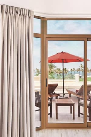 Hotel room at JA Resort with a large window opening to a patio with red umbrella and sea view.