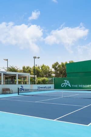 Outdoor tennis court at JA Gallery with blue playing surface, green surroundings, and JA Resorts branding.