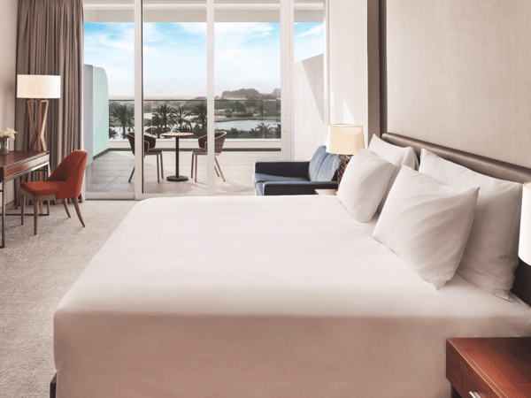 Deluxe room at JA Lakeview Hotel with a double bed, stylish furnishings, and a balcony view of palm trees and water.