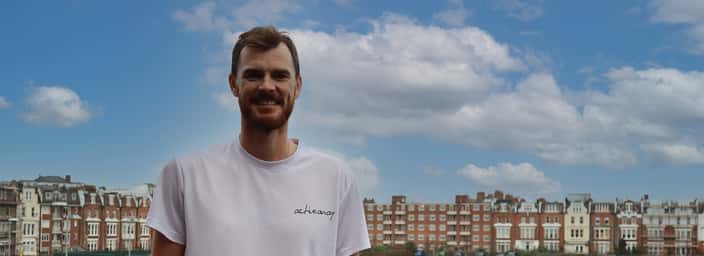 Smiling Jamie Murray wearing an 'Active Away' t-shirt with historic buildings and a blue sky in the background.