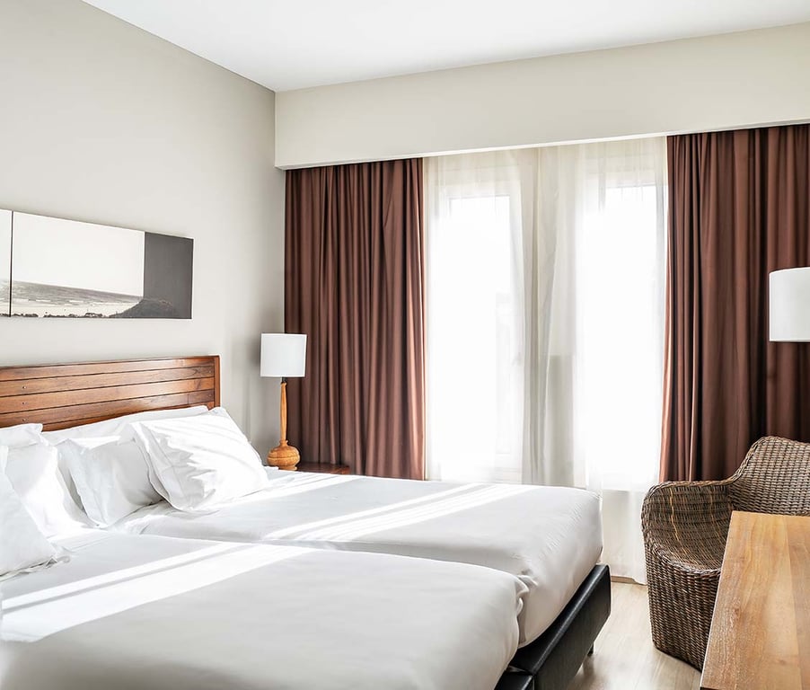 Junior Suite at Hotel Vincci with twin beds, white linens, wooden headboards, and large windows with brown drapes.