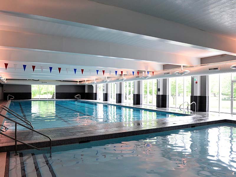 Indoor swimming pool at The Lensbury with large windows, black and white tiling, and colourful triangular flags overhead.