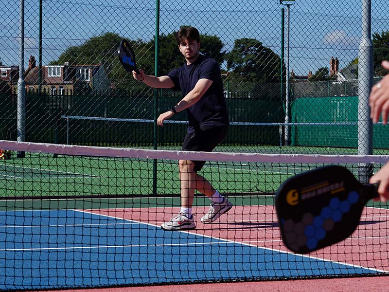 Young tennis player holding a paddle on an outdoor court during a junior tennis camp at The Lensbury.