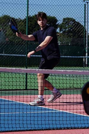 Young tennis player holding a paddle on an outdoor court during a junior tennis camp at The Lensbury.