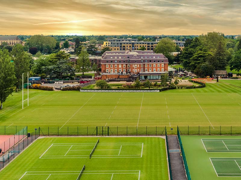 Aerial view of tennis courts and The Lensbury hotel surrounded by greenery.